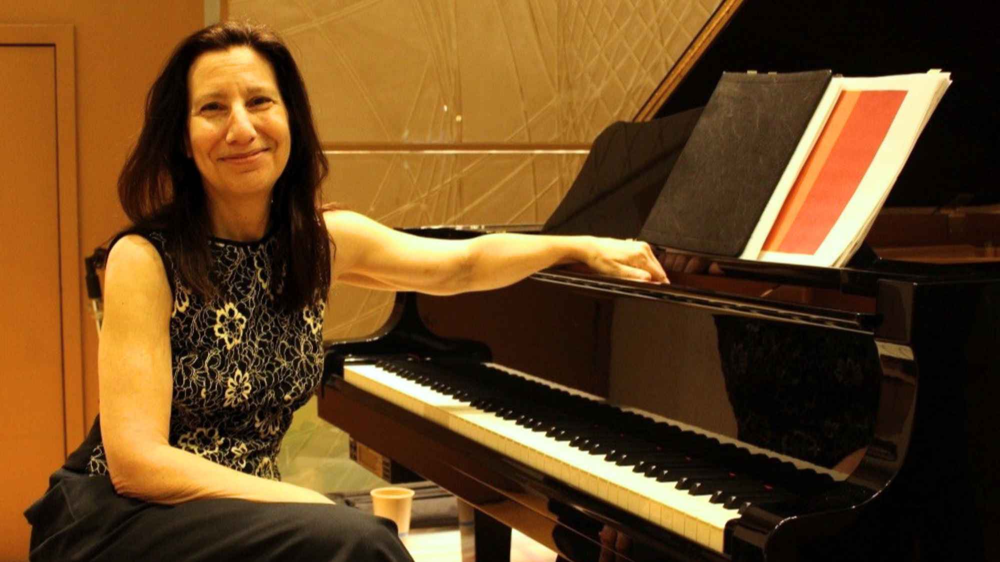 A woman with dark hair sits at a piano smiling