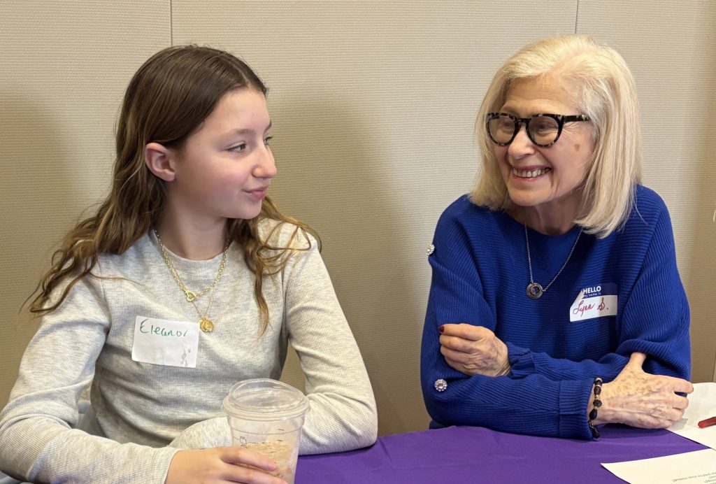 A young girl and older woman sit at a table smiling at each other