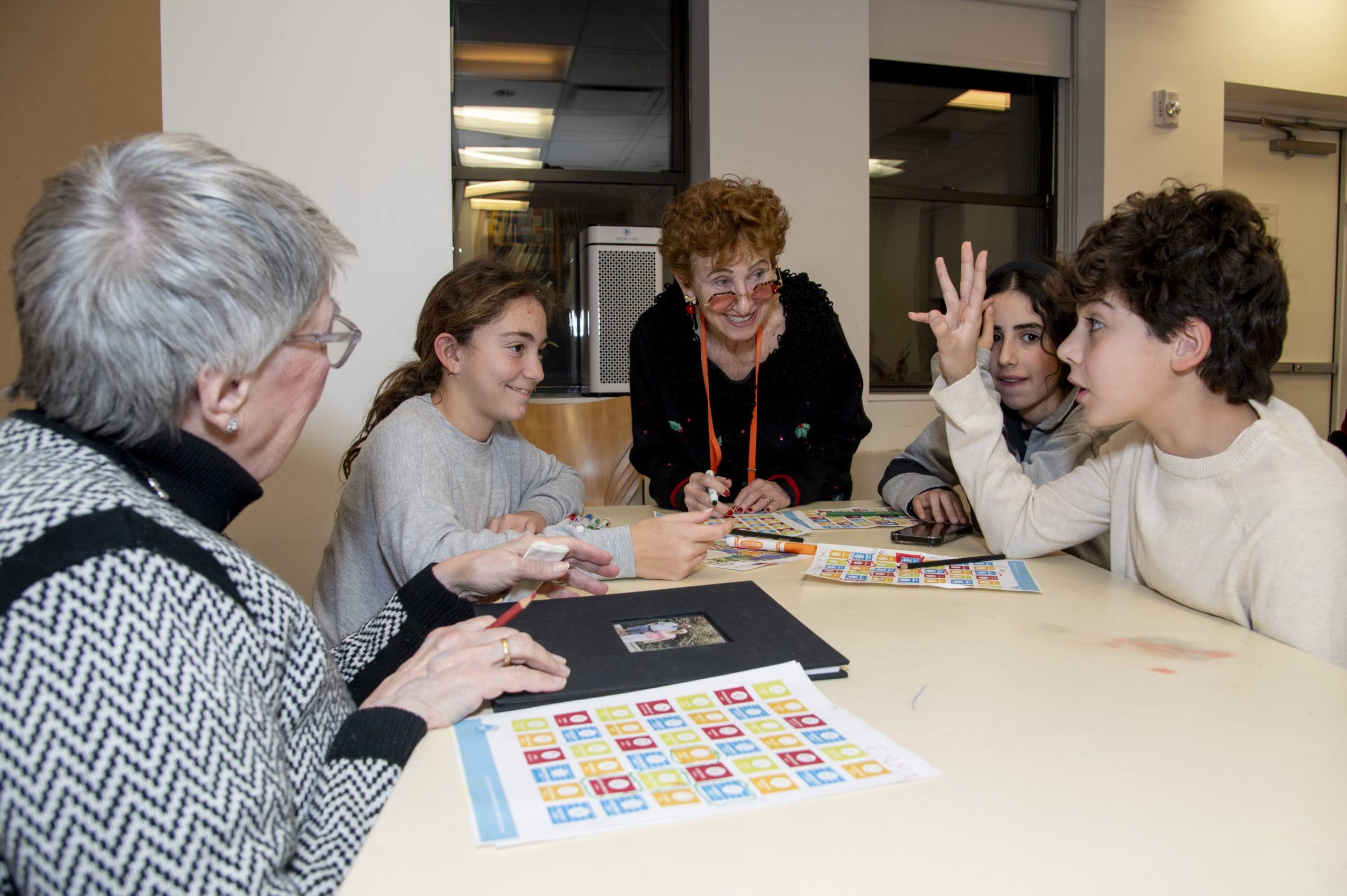 Three b-mitzvah aged youth engaged in conversation with two older adults at DOROT.