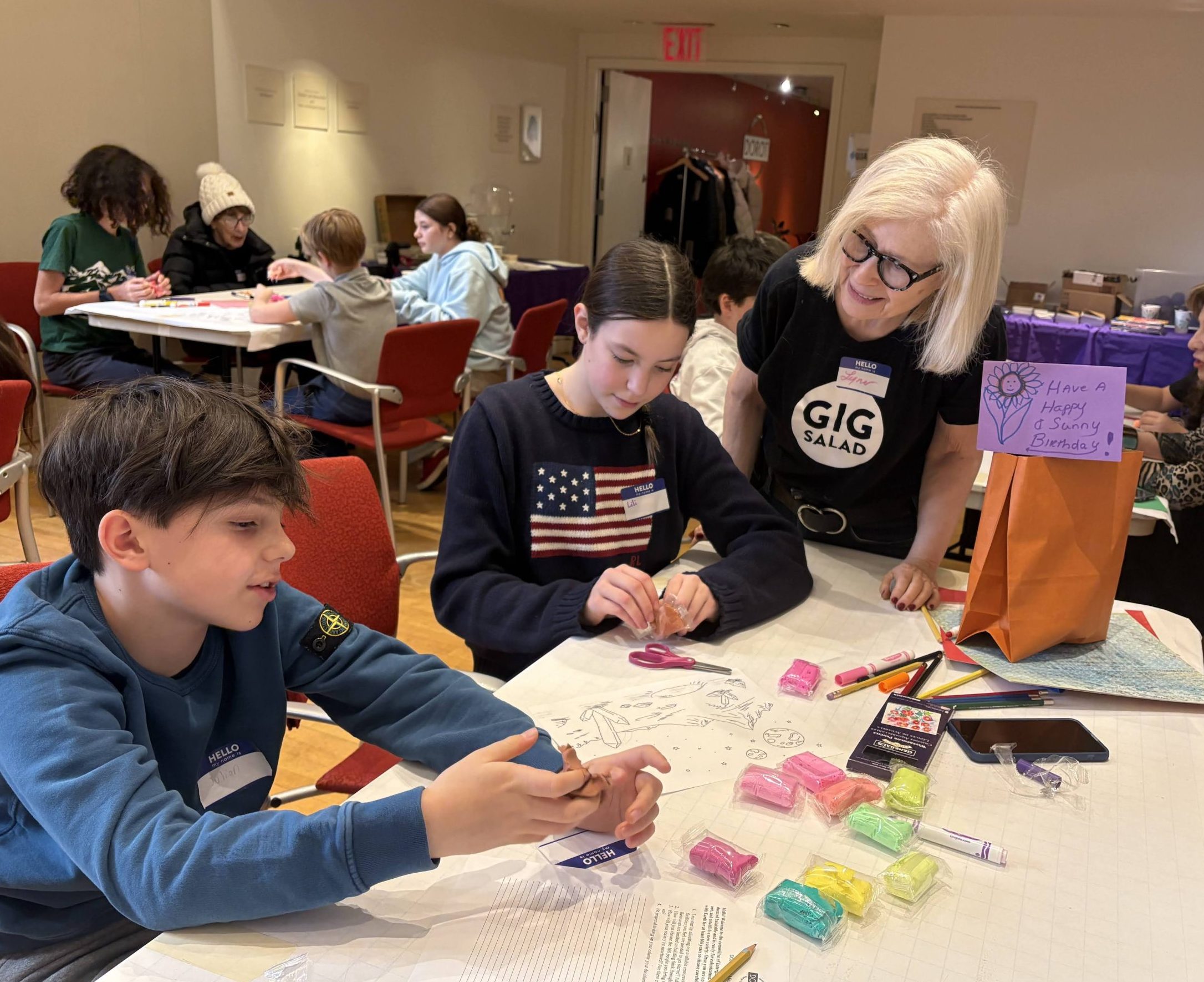 A young boy and girl at a table doing an activity while an older woman smiles and talks with them.