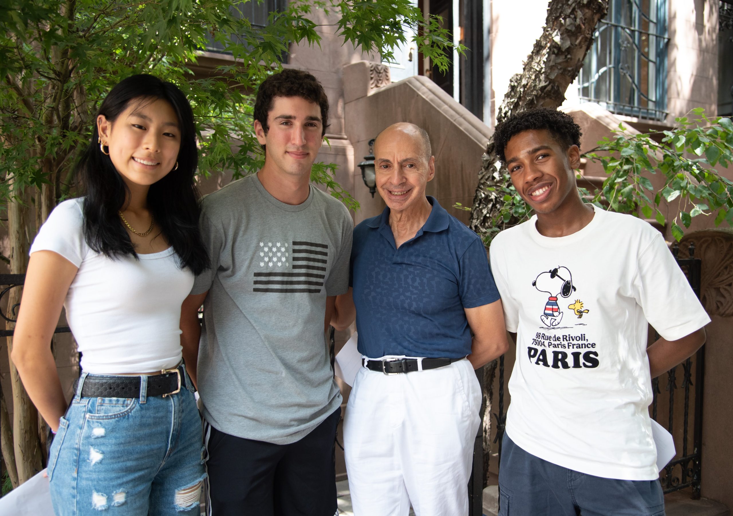 A group of three teens and one older man stand next to each other on a new york city street
