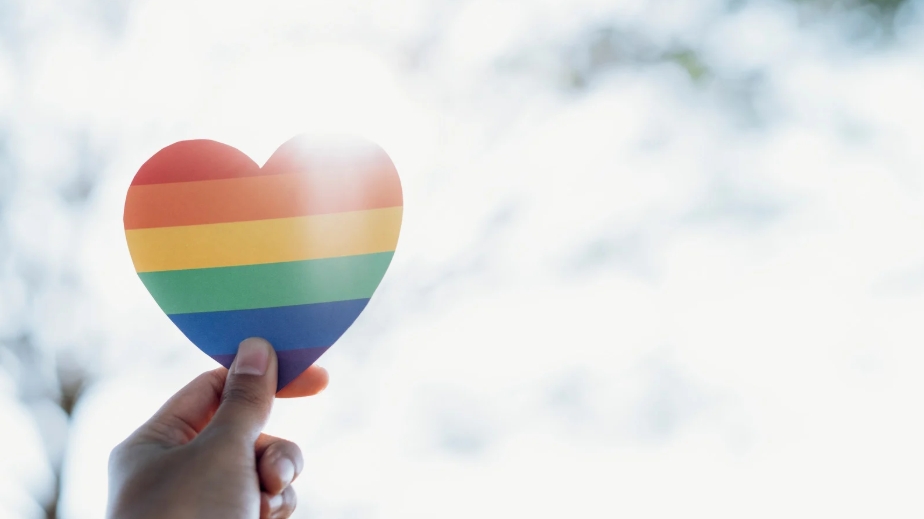 A picture of a hand holding a rainbow heart, symbolizing a place for LGBTQ+ support.