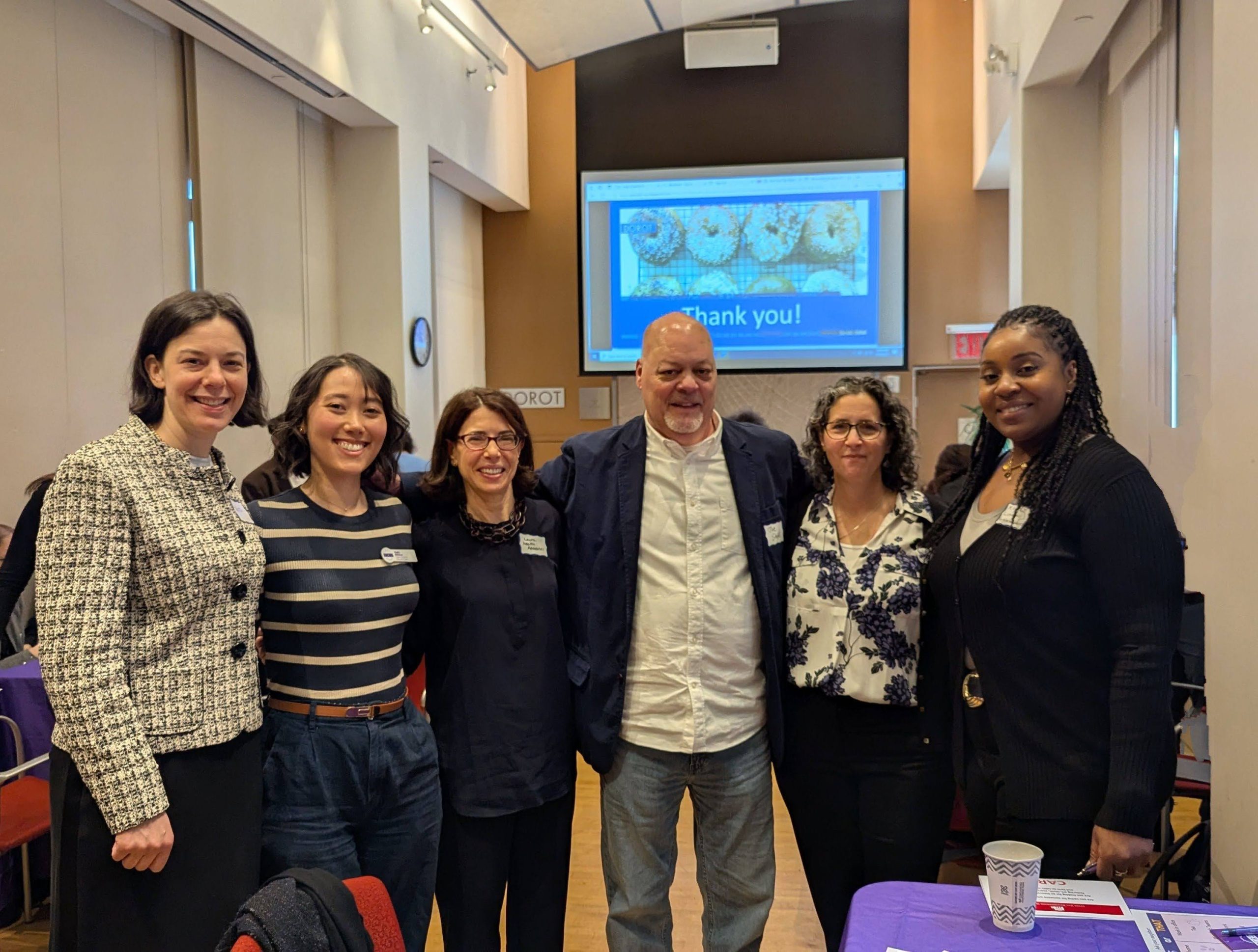 A group of people from partner organizations and DOROT staff stand arm in arm smiling at DOROT