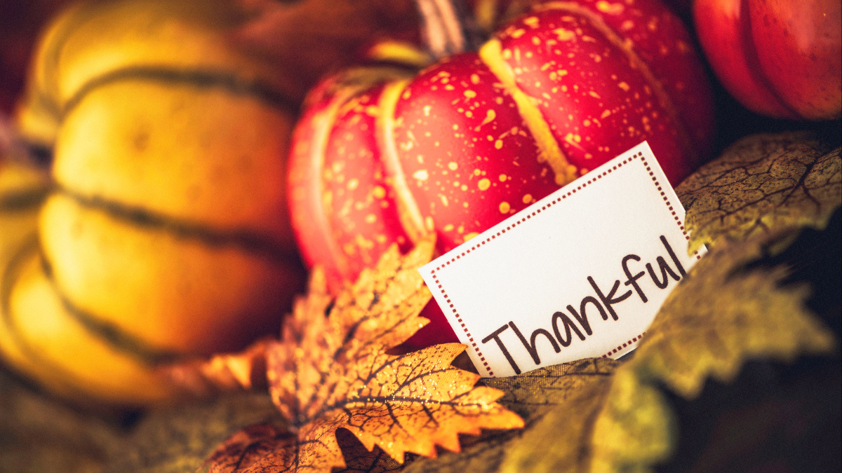 Pumpkins with fall leaves with a note reading "thankful."