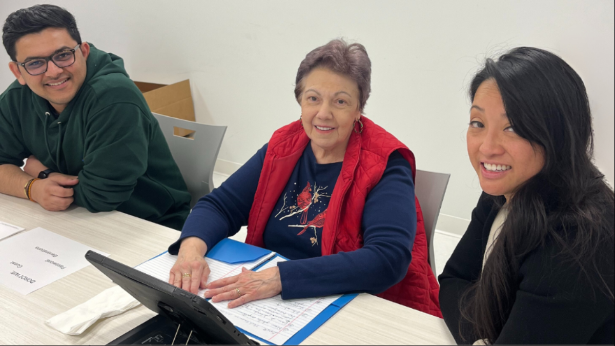 Two DOROT volunteers sit on either side of an older adult using a laptop.