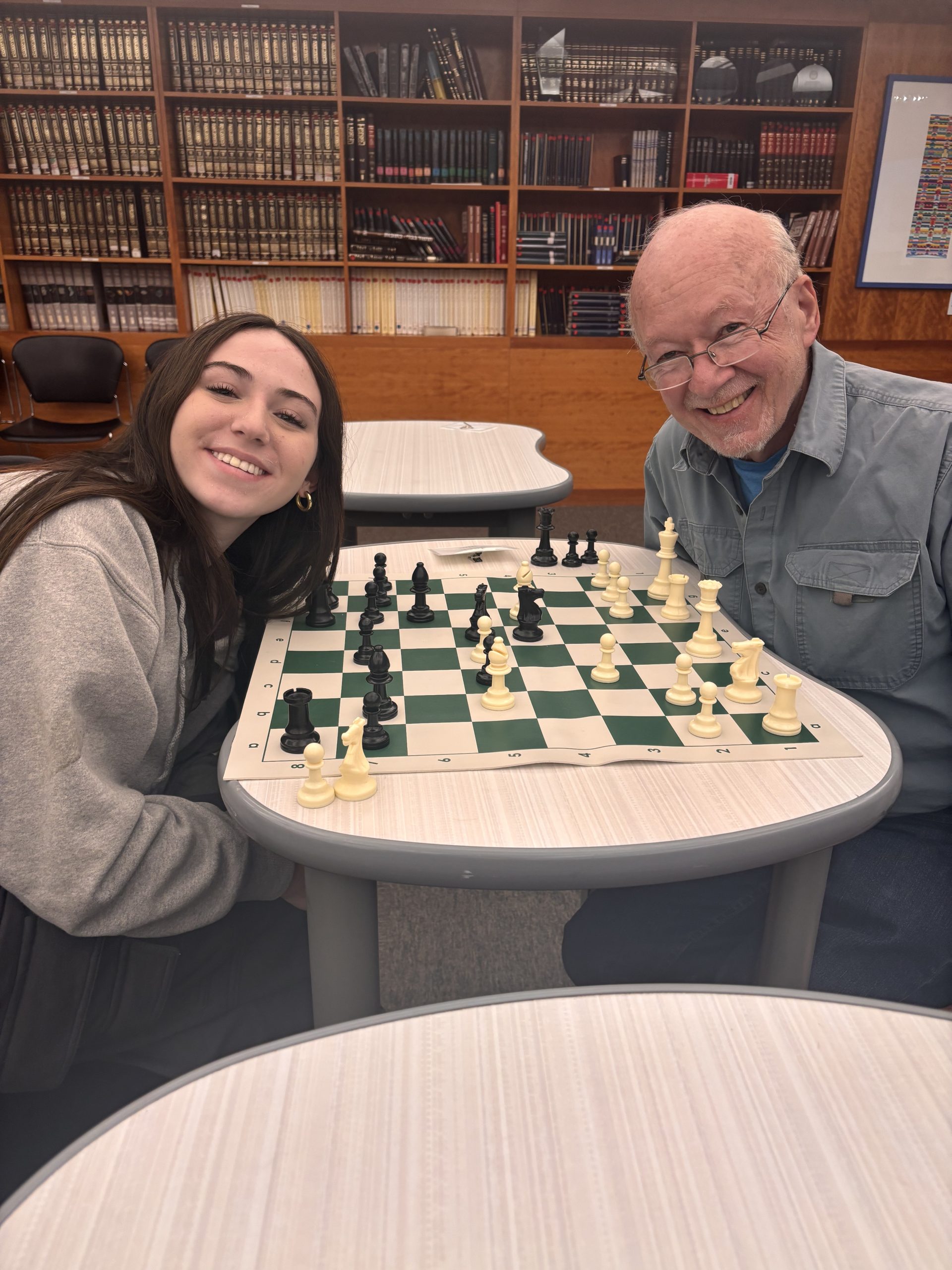 An older adult and teen smile while they play a Chess game.