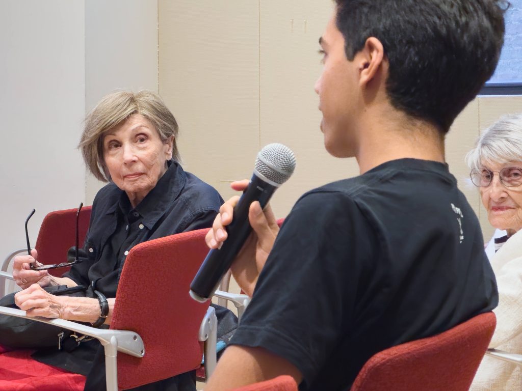 A teen speaks into a microphone as two older adults listen intently.
